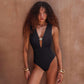 Front view of a model wearing the black deep-V swimsuit with gold-tone detail.